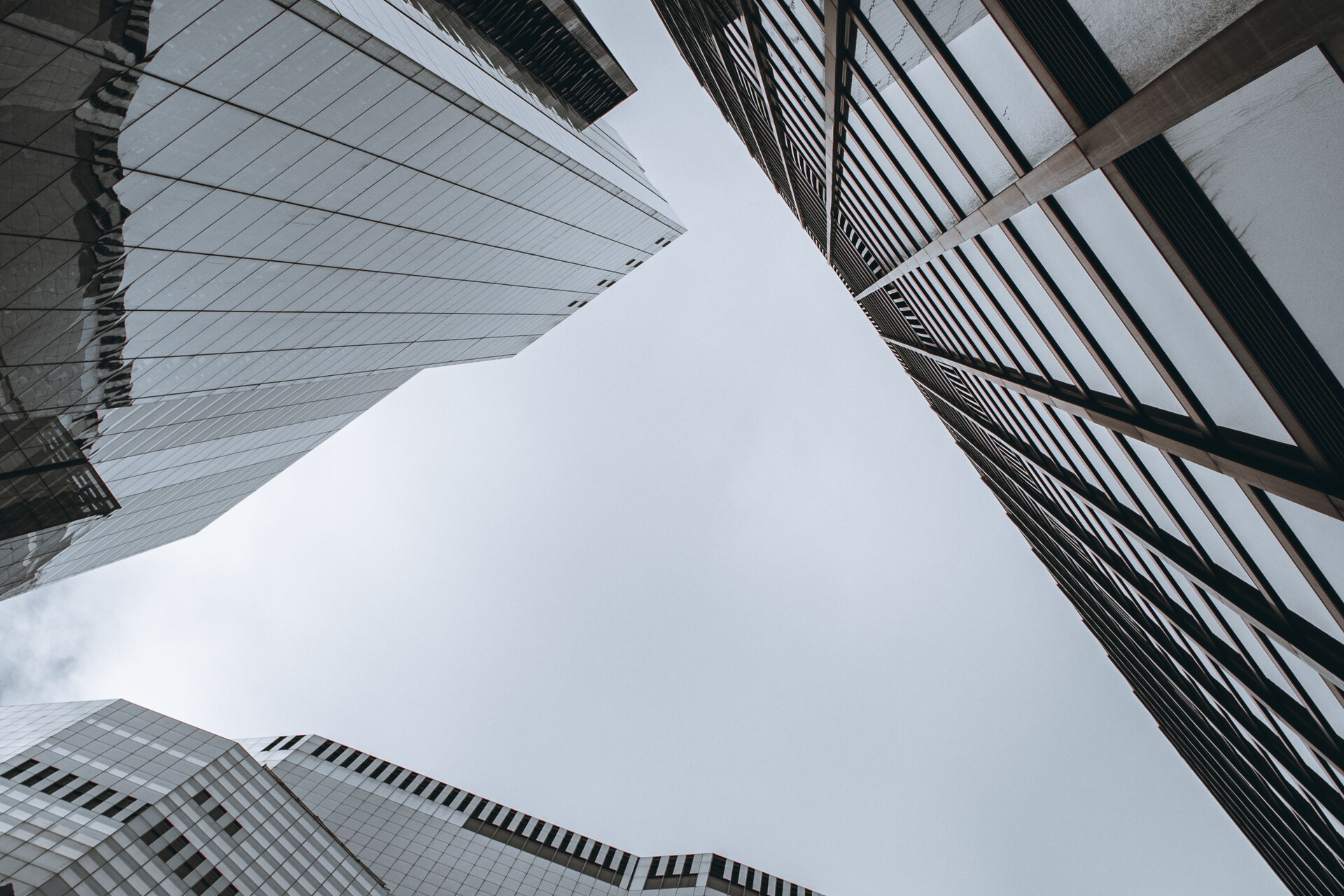 Upward view between glass and steel skyscraper facades beneath an overcast sky